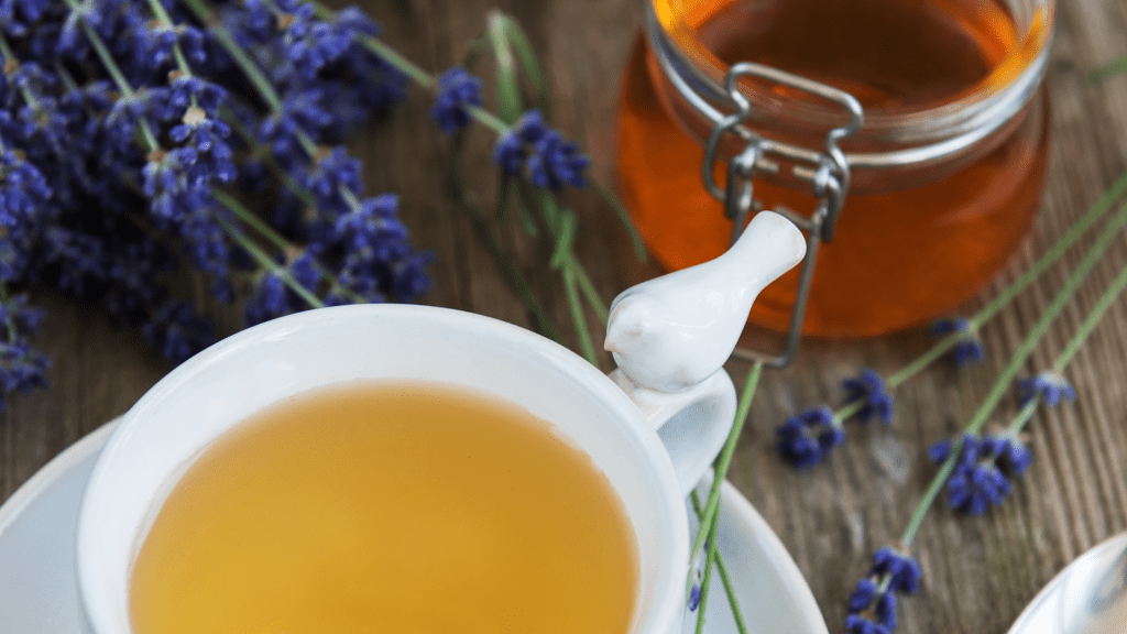 Cup of lavender honey tea with dried lavender flowers and honey jar on a wooden surface